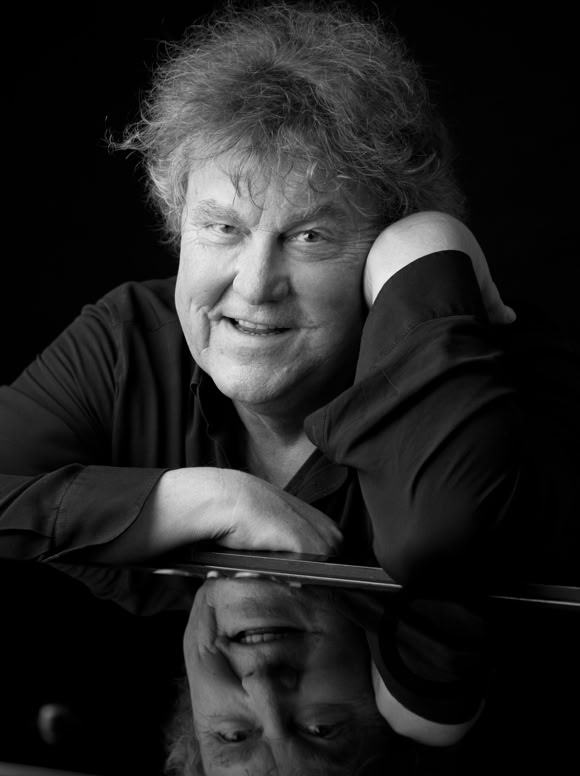 Schwarz-wei&szlig;-Foto von Lutz G&ouml;rner, der sich auf einen Tisch lehnt und l&auml;chelt, mit einer Spiegelung auf der Tischoberfl&auml;che.